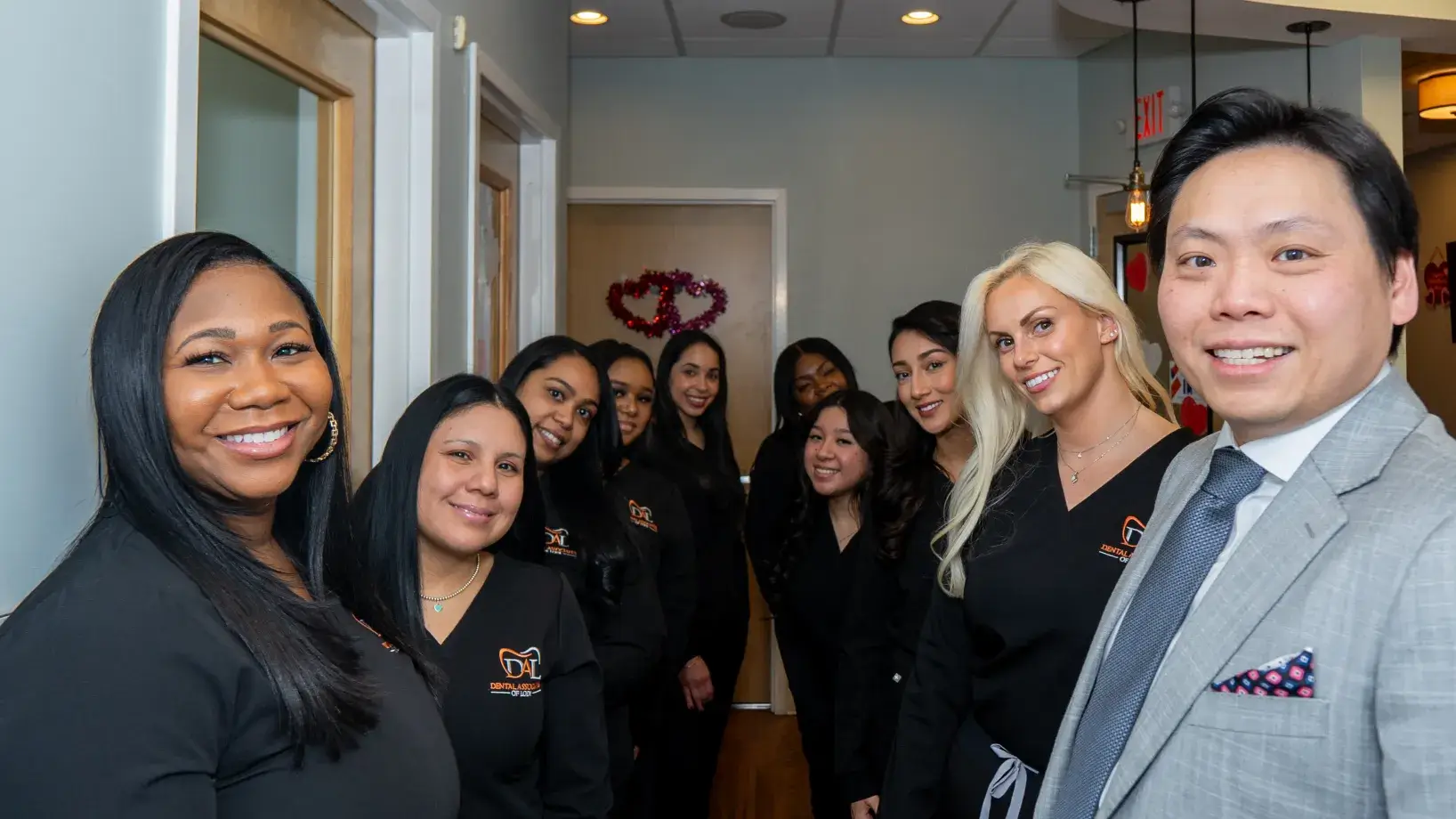 A group of smiling people wearing professional attire stands together in a hallway.