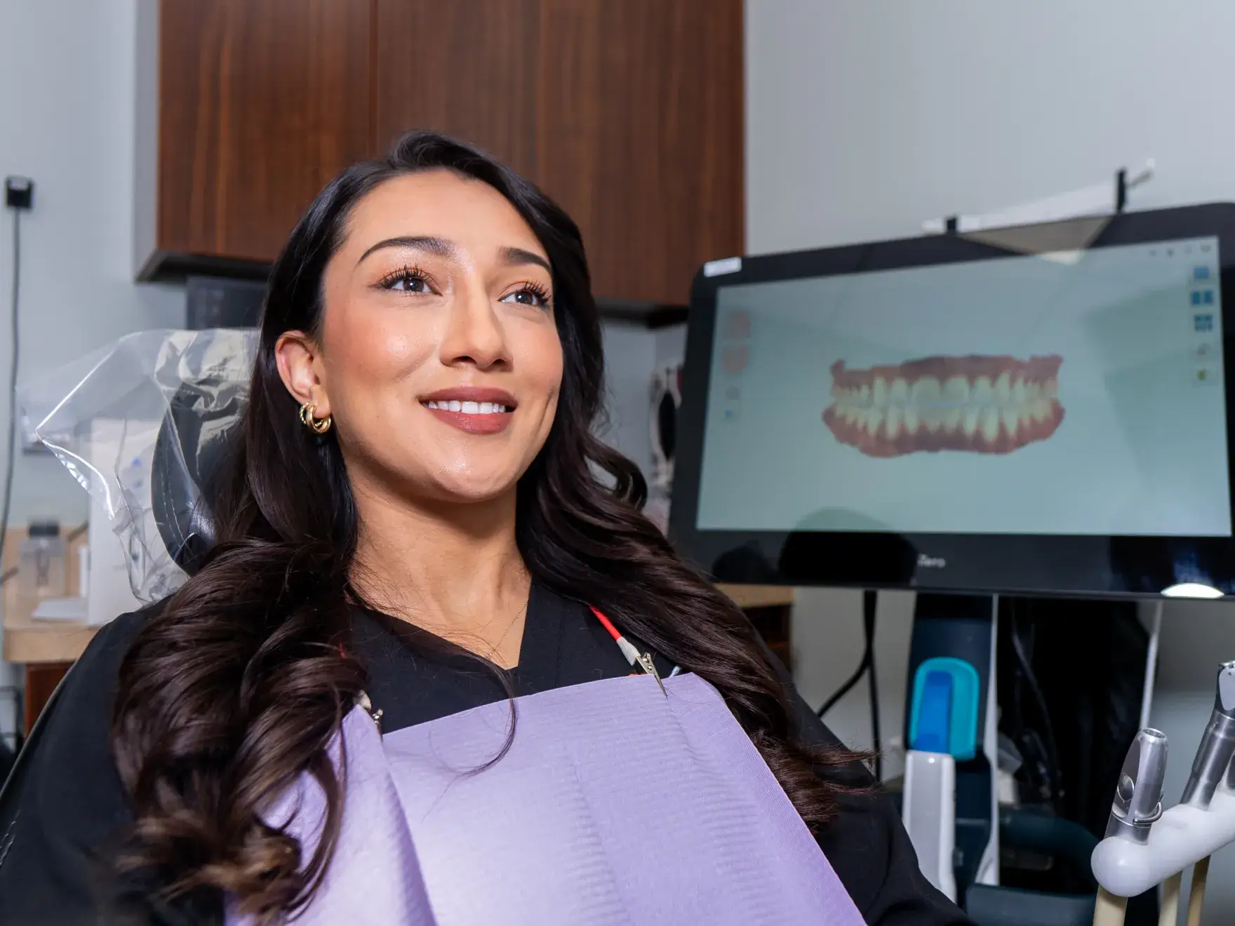 A woman seated in a treatment chair beside a digital dental model.