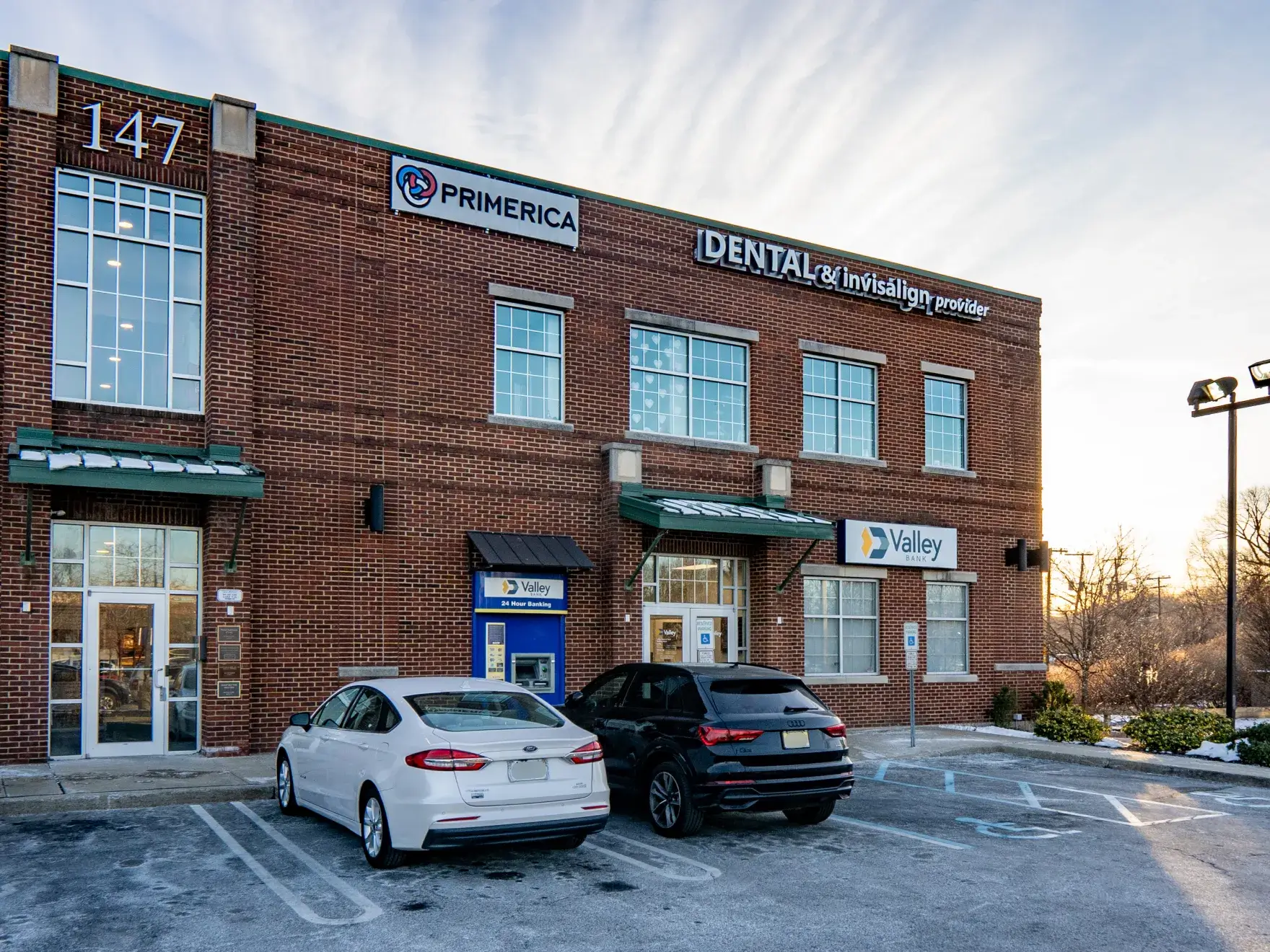 Two parked cars in front of a brick building with signs for Dental, Primerica, and Valley.