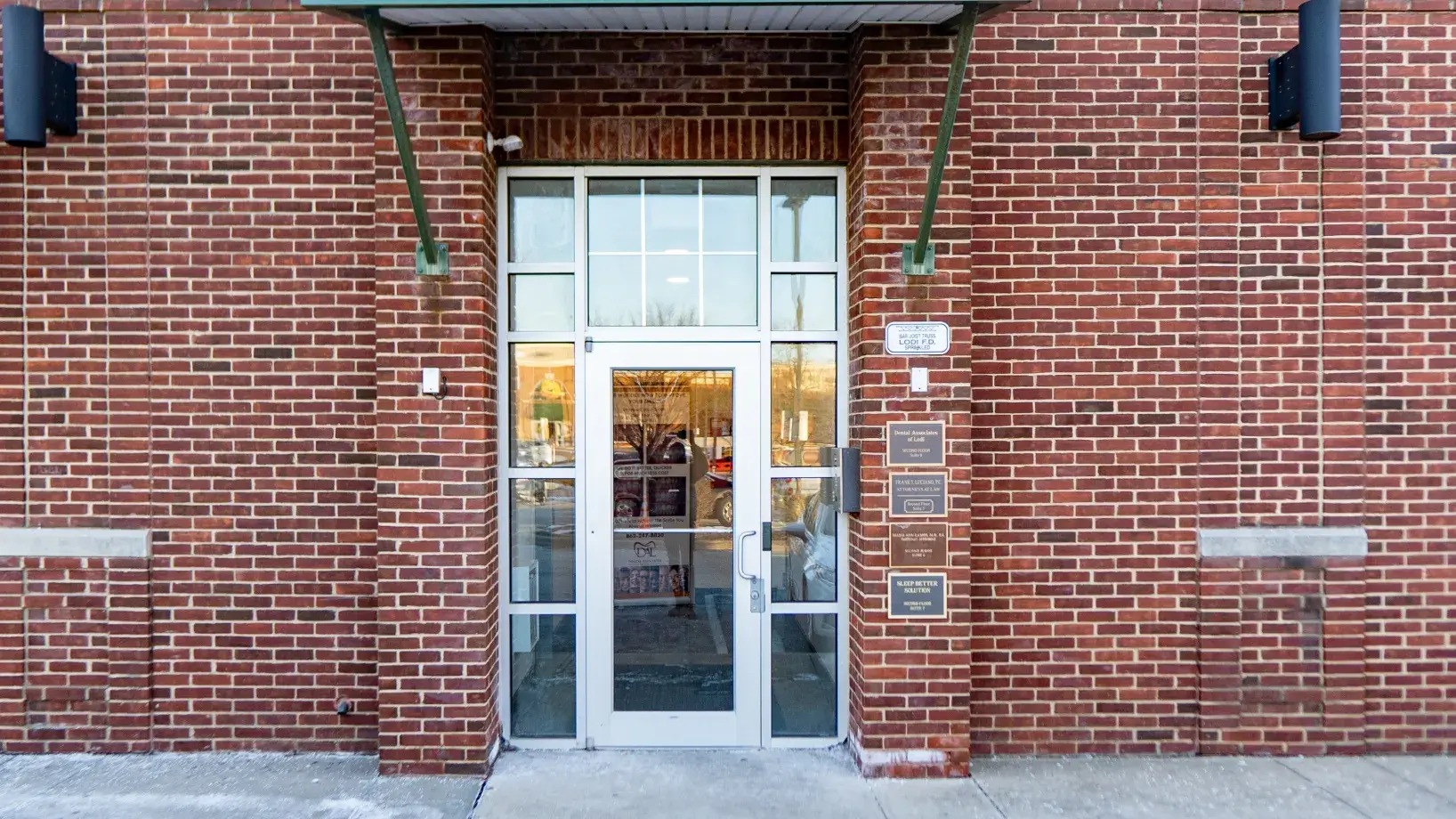 Glass door entrance set in a brick building with multiple business plaques on the right side.