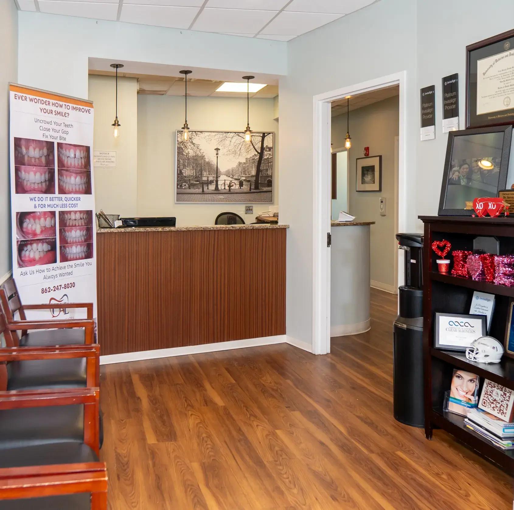 Dental office reception area with wooden desk, three chairs, teeth improvement banner, and decorative shelf with red heart ornaments.