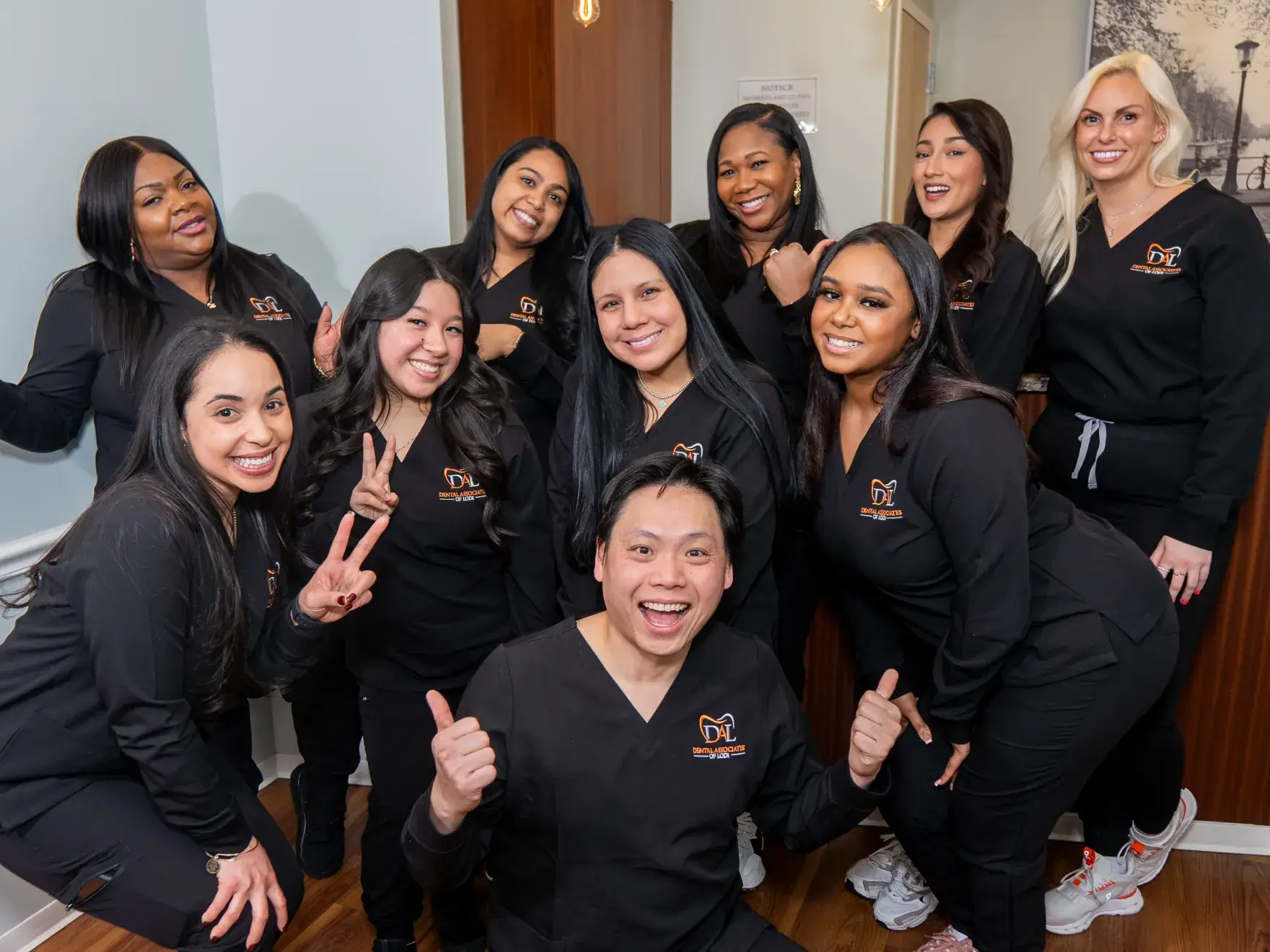 A group of smiling people wearing matching black uniforms pose together, some making thumbs-up gestures.